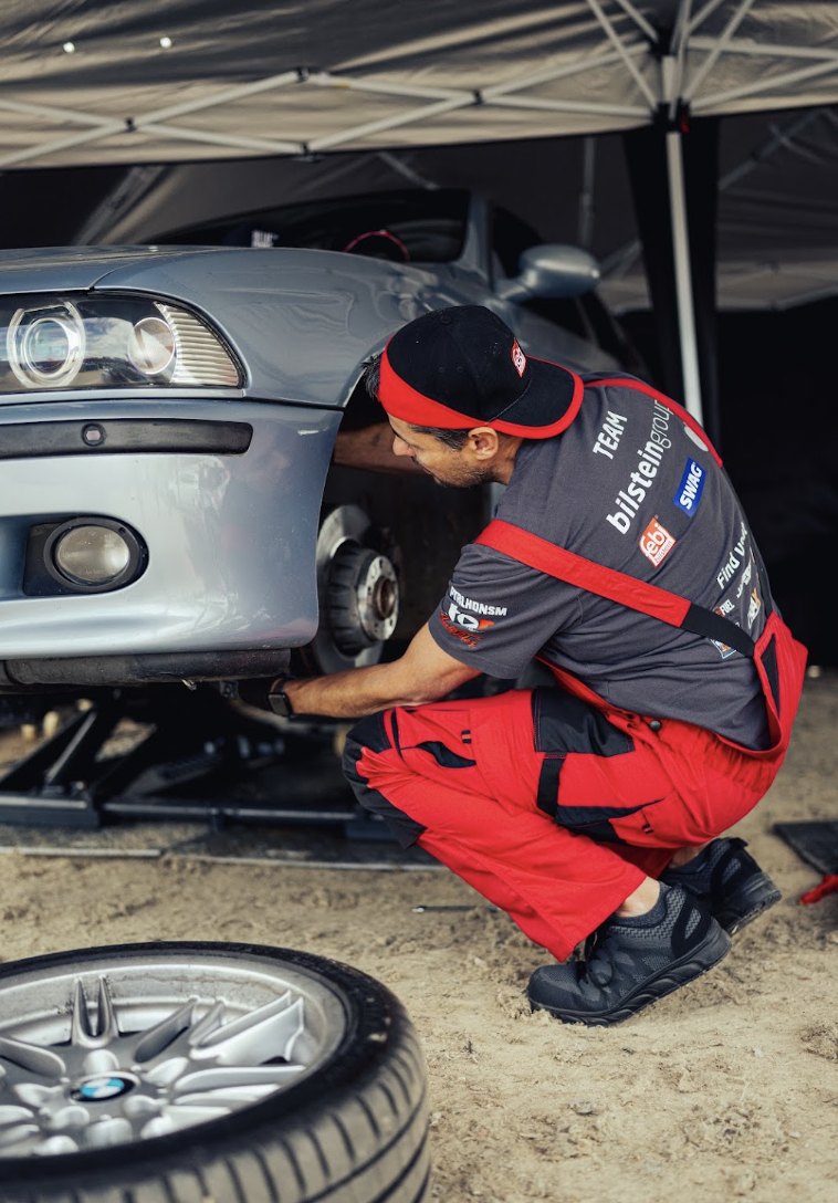 A febi bilstein team mechanic working on a BMW's front brakes in the pit tent